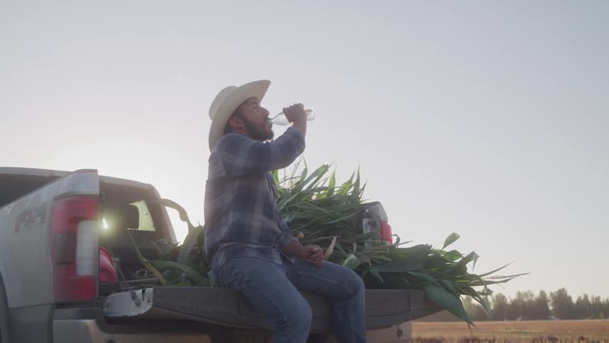 Man sitting in the trunk of a pickup truck drinking water