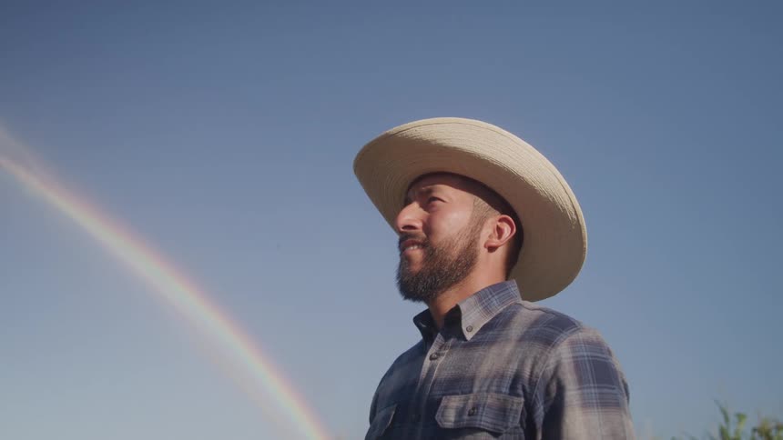 Bearded man with a hat outdoors with a rainbow in the background