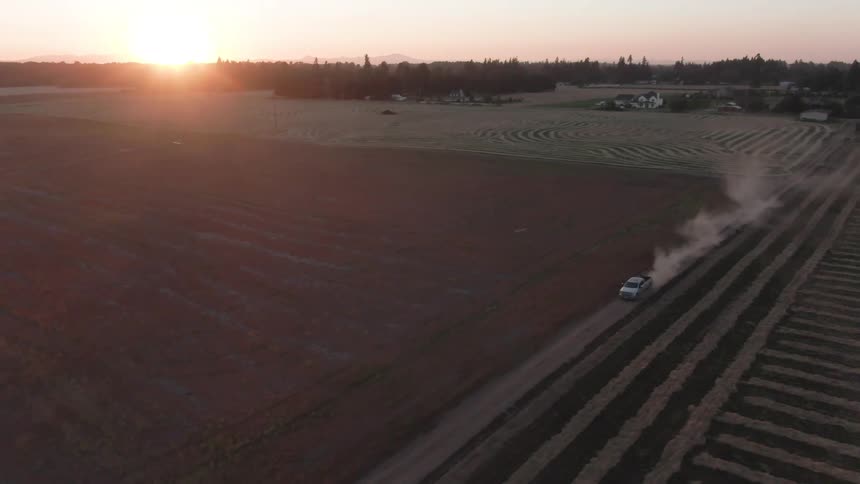 A truck drives along a field at dusk