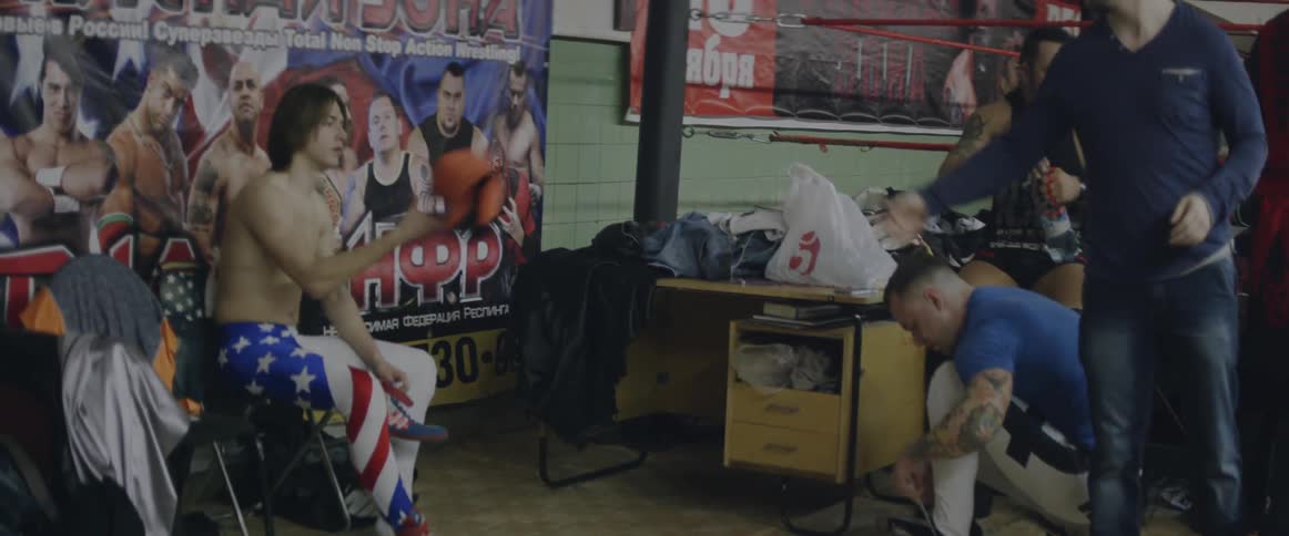 A man sitting in a chair lacing up his shoes while others are preparing themselves as well
