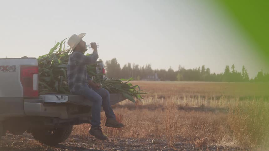A man sits in the bed of his truck and takes a drink of water