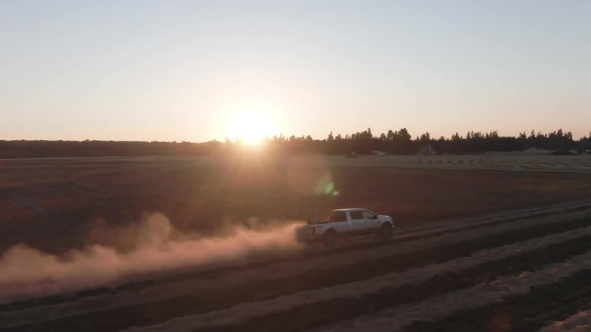 Aerial of a pickup truck riding through a field in a rural area at sunset