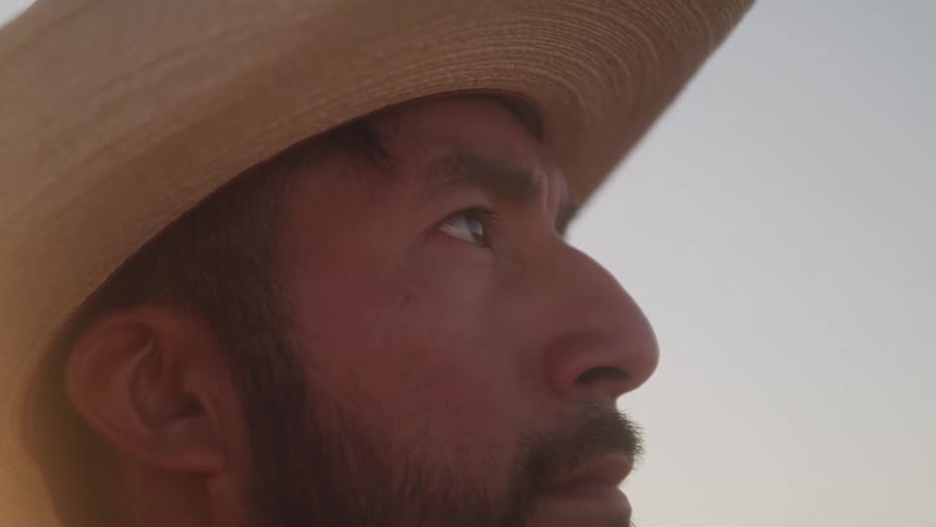 The face of a man wearing a beige hat and staring straight ahead