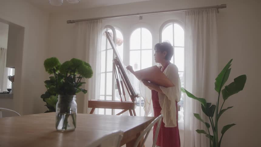 Lady standing in a living room painting a canvas