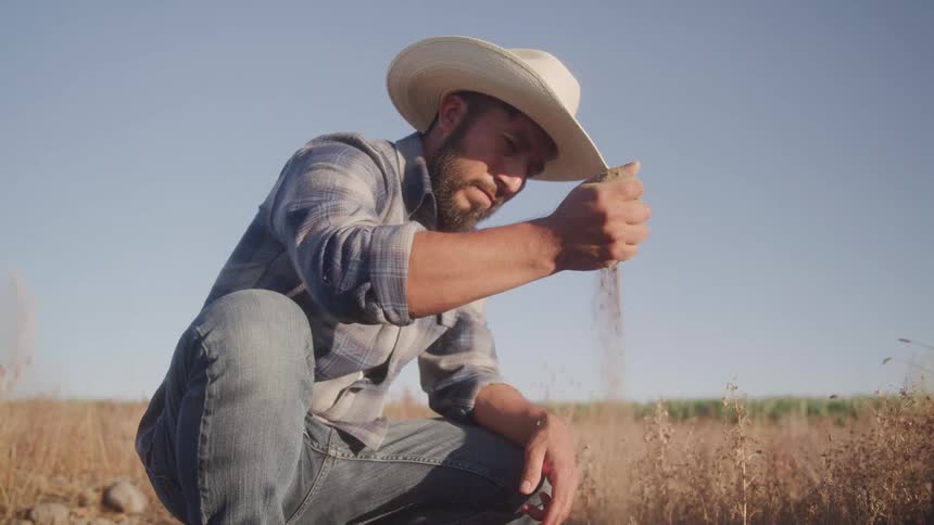 Man in a hat in a farm field releasing soil from his hands