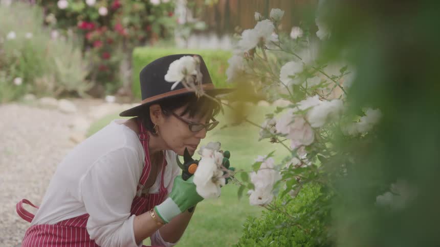 A woman bends down to smell a bush of flowers