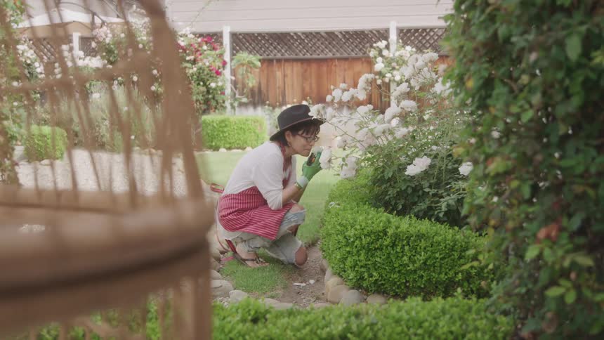 An asian woman perceives a flower while kneeling in a garden during daytime