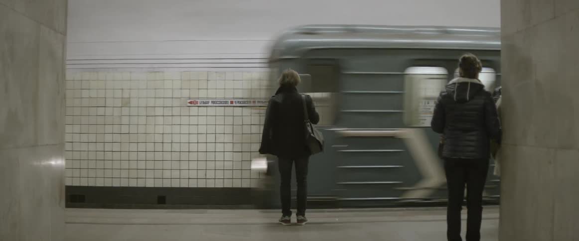 A person standing in a subway station holding a bag and waiting for the subway