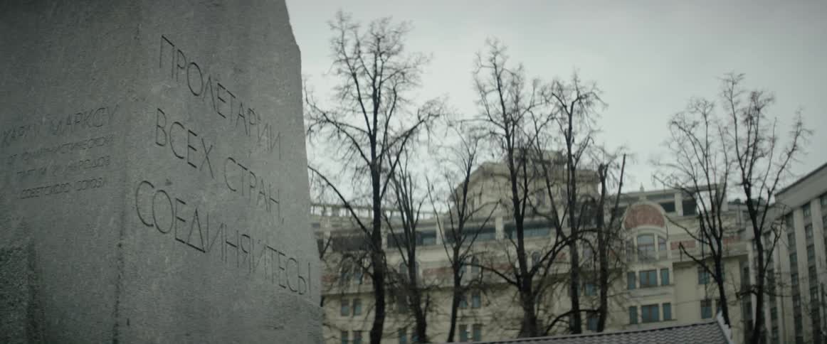 A memorial plaque stands in front of some trees and a building