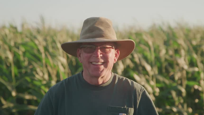 Cheery famer in a sun hat standing outdoors in front of his crops