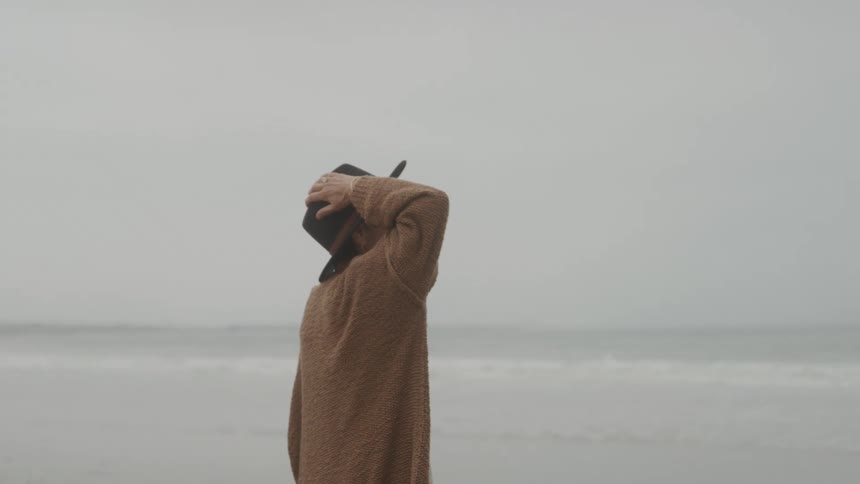 Woman with one hand on her hat while walking along the beach