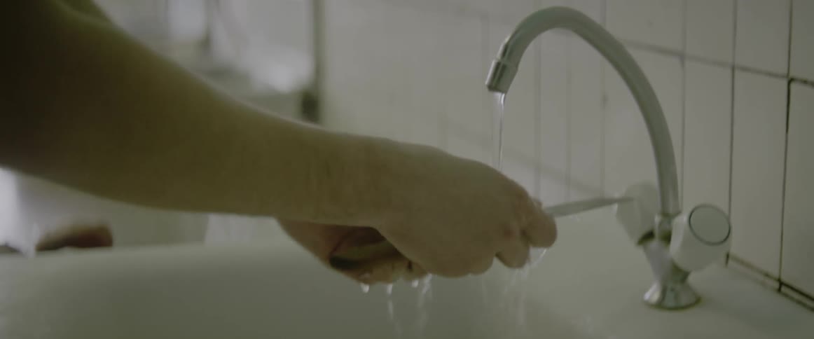 A person holding a potato and knife under water in the sink getting ready to peel it