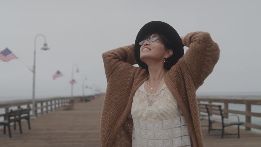 Woman with happy expression putting hands on head while standing in a dock environment on the beach