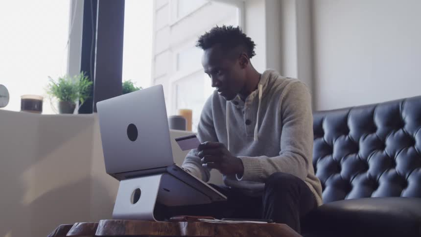 Man sitting holding a credit card and typing on a laptop