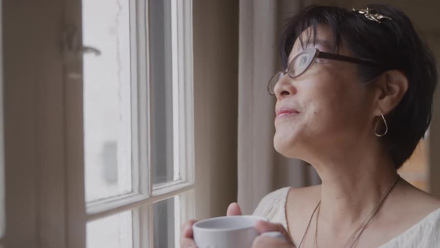 Woman with glasses holding a mug and looking in the window with a happy expression