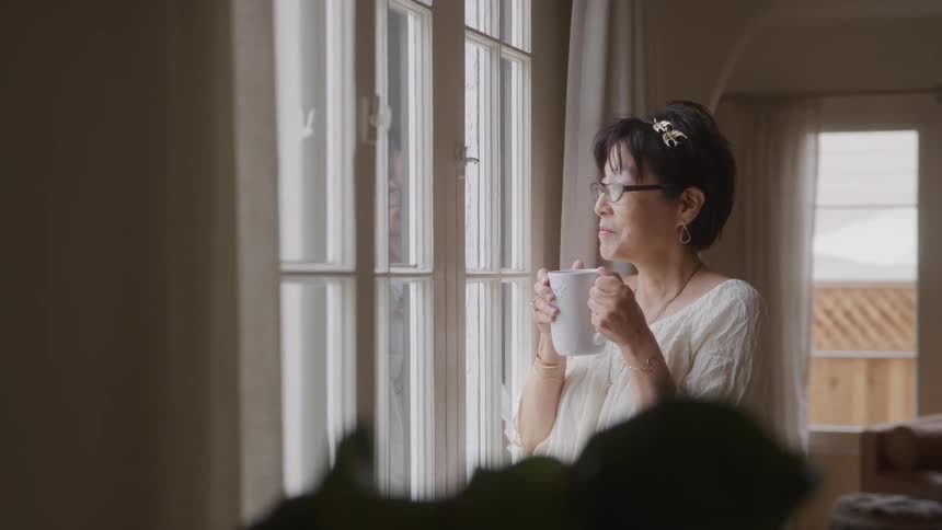 Woman enjoys her coffee by the window while looking outside