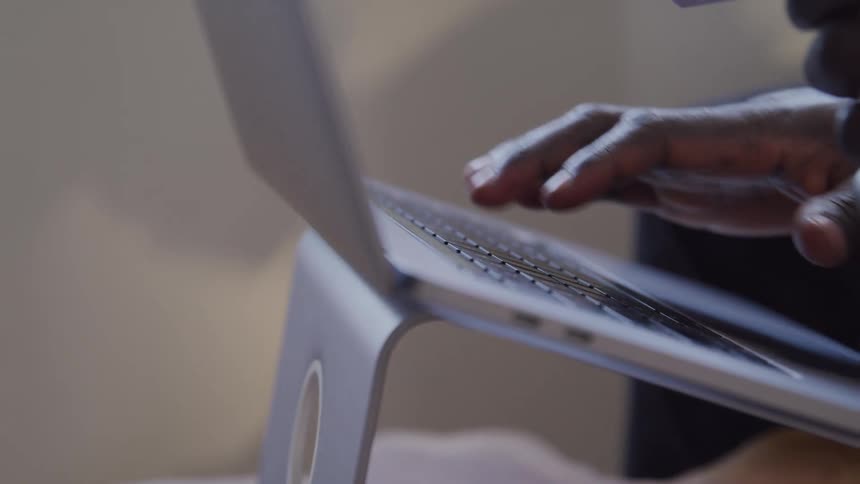 A man types on his laptop keyboard at midday