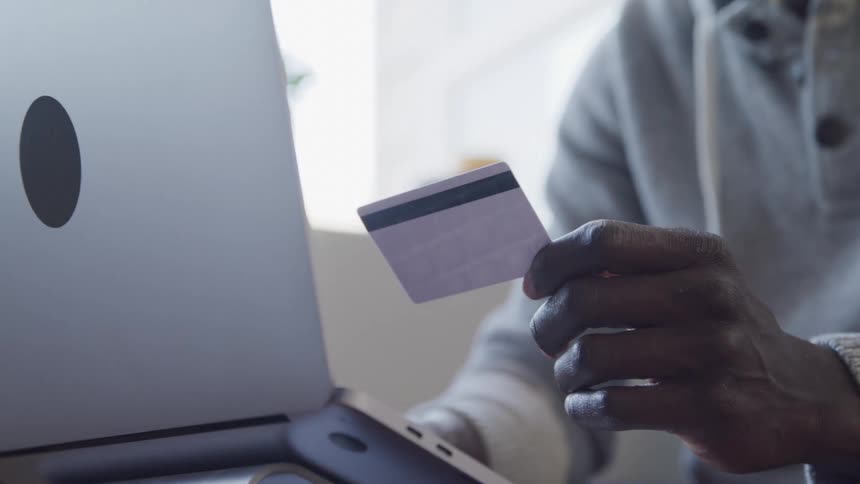 Person holding a card while typing on a laptop