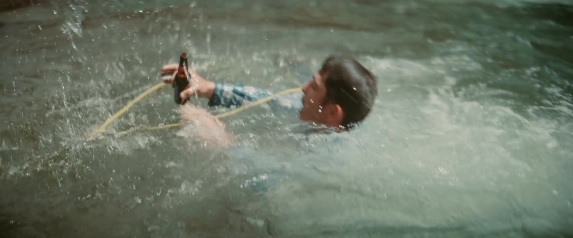 A man swings a rope over to another man swimming in a river to pull him out with a horse standing nearby in the woods at midday