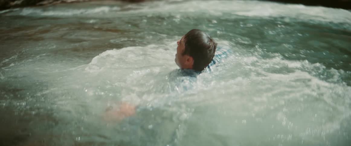 A man swimming in a river struggling to stay afloat while holding a bottle at midday