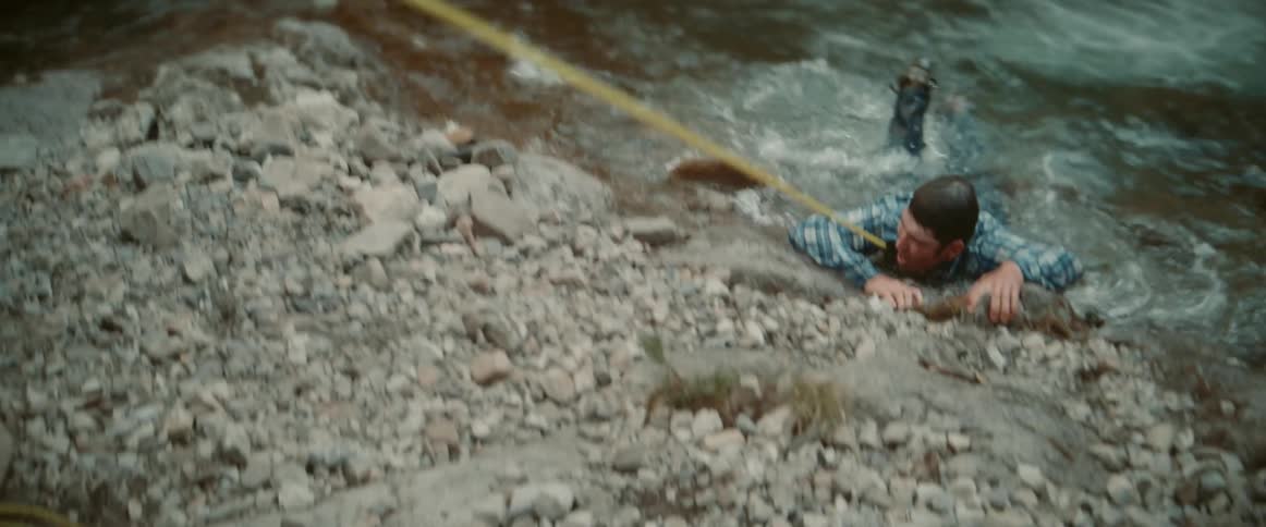 Cowboy uses a lasso to rescue a man drowning in a rushing river while a horse stands nearby