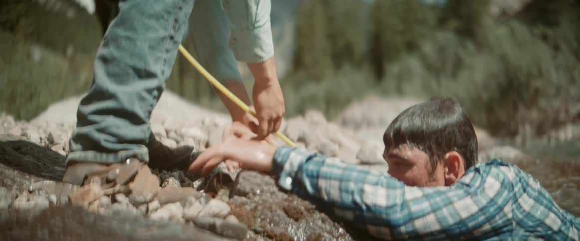 Cowboy sitting on a horse uses a lasso to rescue a man drowning in the river