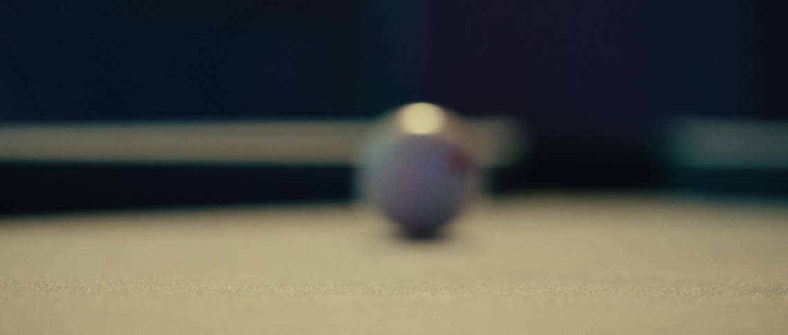 A person hits an 8ball with a cue ball on a pool table the shot is low to the ground focusing on the movement of the balls