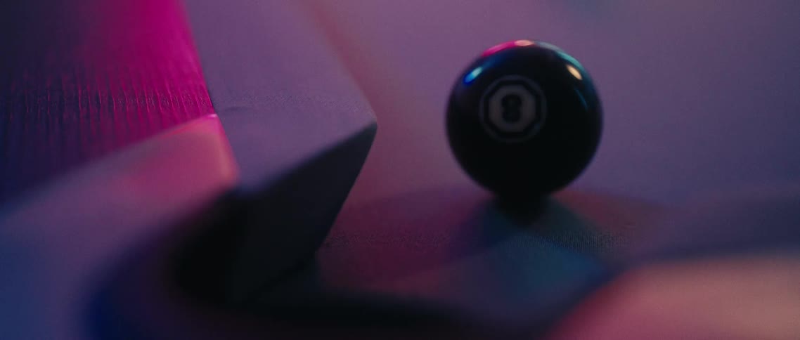 The white ball hits the black 8ball on a pool table sending it down the pocket