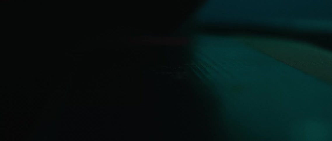 A black rectangular object sits on a dark green surface with a faint blue light in the background the lighting creates a mysterious and abstract atmosphere