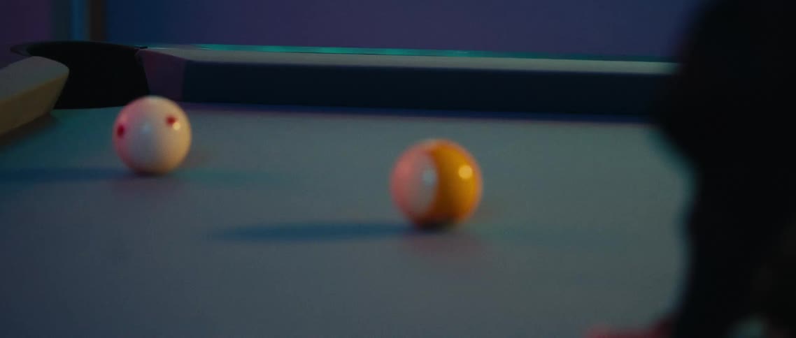 A closeup shot of a pool table shows the cue ball making contact with another ball with other colored pool balls scattered on the blue felt surface