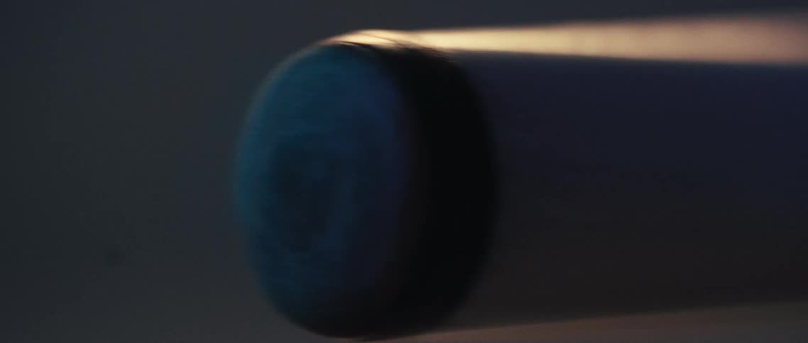A closeup shot shows a pool cue highlighting its tip and the shaft as it moves the scene is dimly lit emphasizing the texture of the cue stick