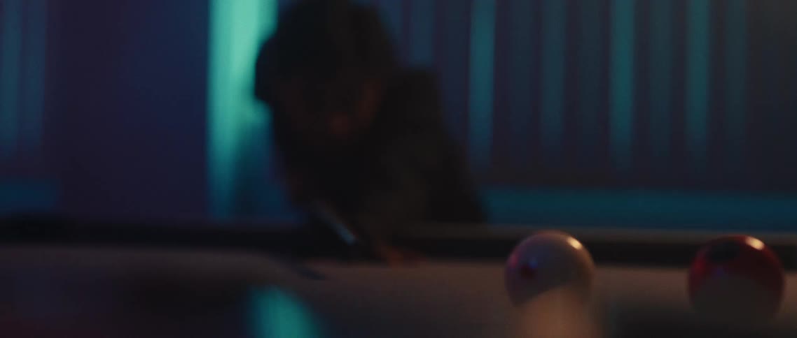 A pool player concentrates and hits the white ball displacing other balls on the pool table