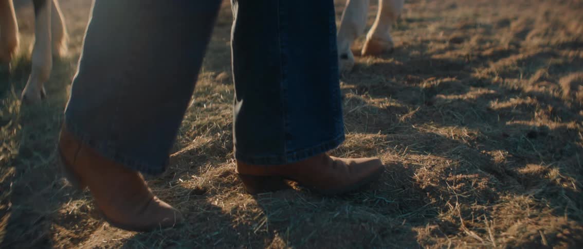The woman is walking past the horses on the ranch