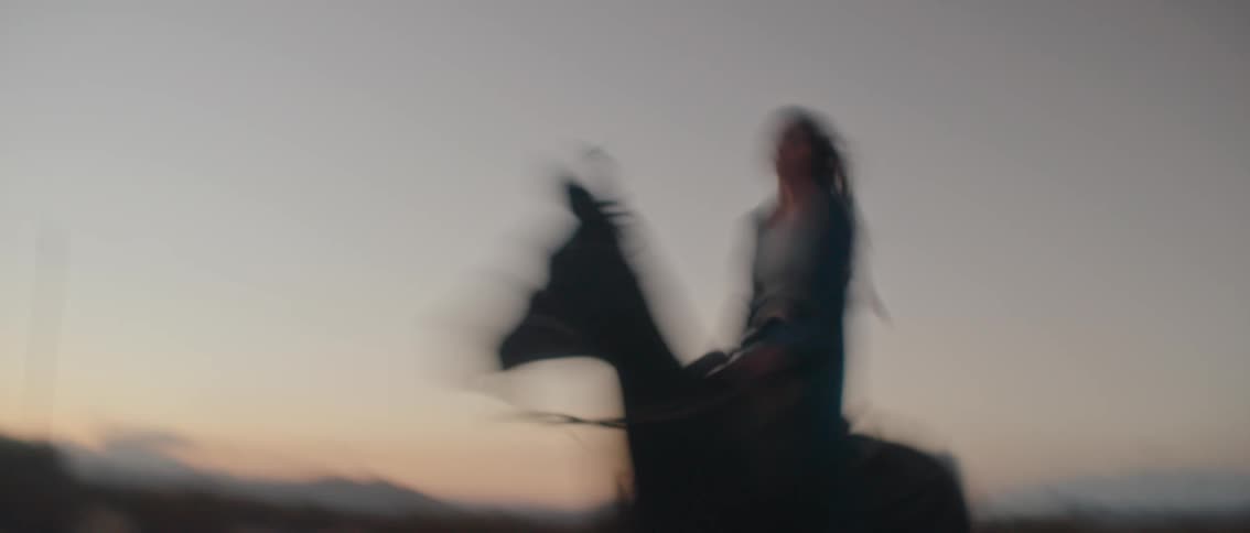 A lone rider on a dark horse is seen galloping through a vast open desert landscape at dusk the scene conveys a strong sense of freedom and the wild untamed spirit of the american west