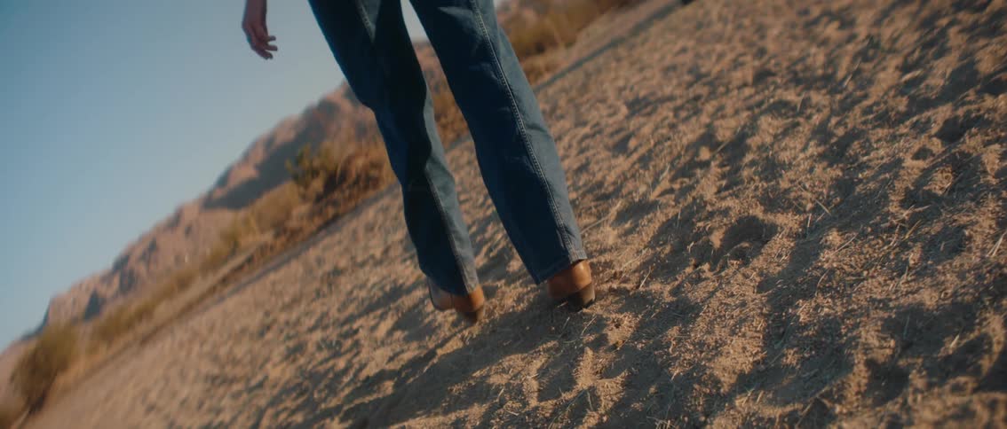 A determined individual clad in jeans and boots struggles to walk uphill on a dusty sandy slope their boots kicking up clouds of dirt with each step