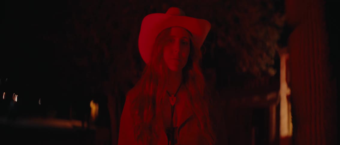 A striking portrait of a woman wearing a cowboy hat illuminated by a deep red light staring intently at the camera with a captivating and mysterious expression