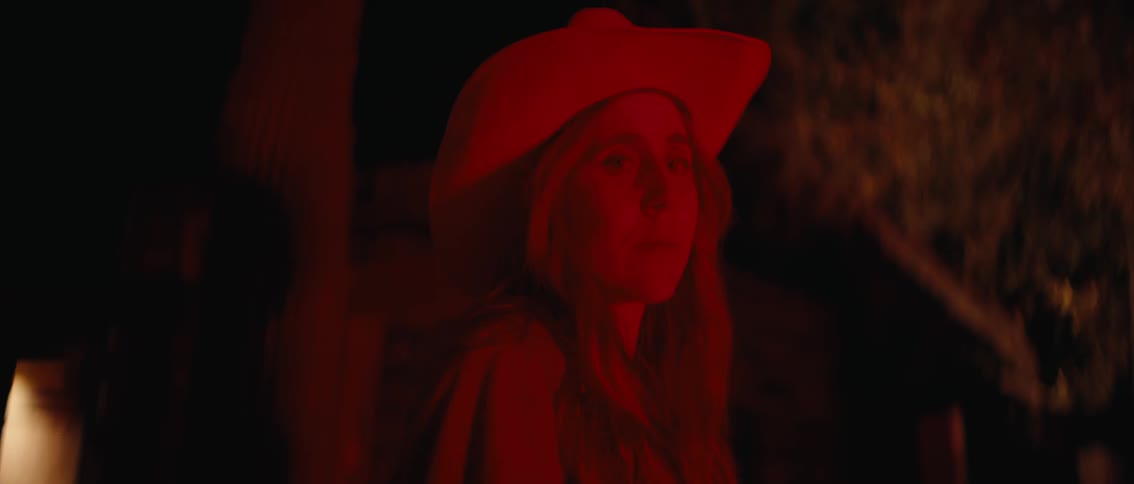 A captivating redlit closeup of a woman in a cowboy hat as she slowly raises her head and looks upward with a mysterious expression