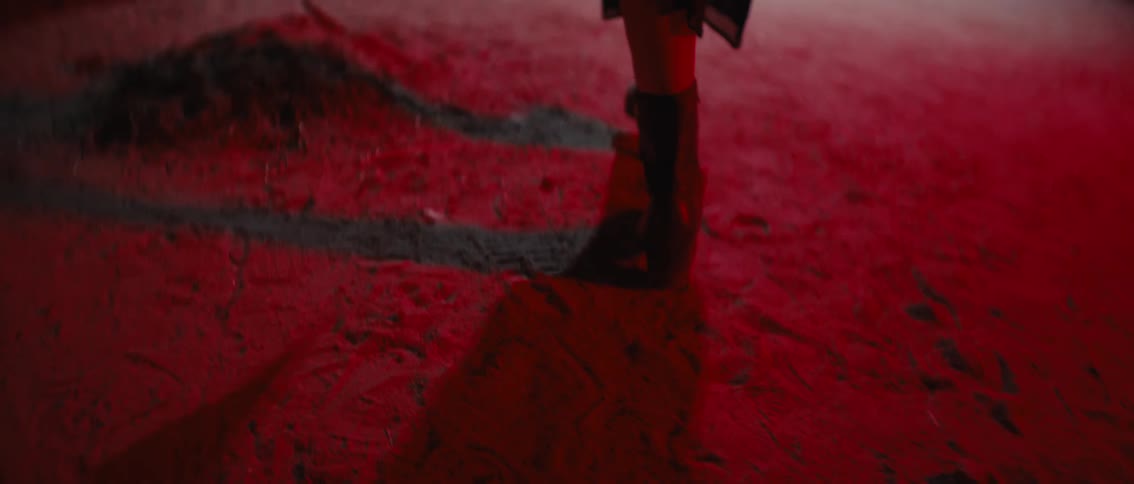 The video features a closeup of a persons legs in dark boots walking across a textured red surface casting prominent shadows the strong red color and visible texture create a sense of depth and focus on the movement