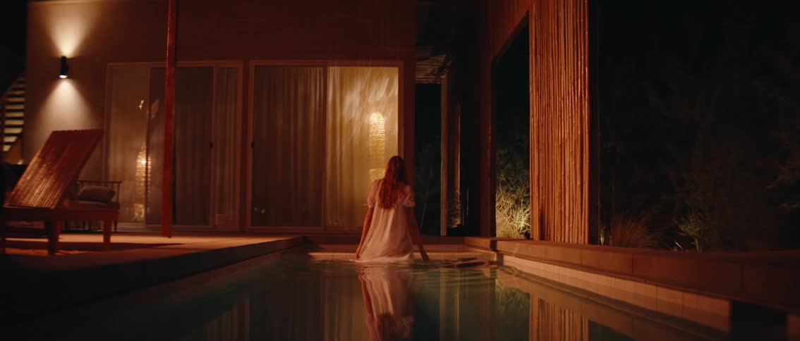 Woman in white dress entering a swimming pool at night