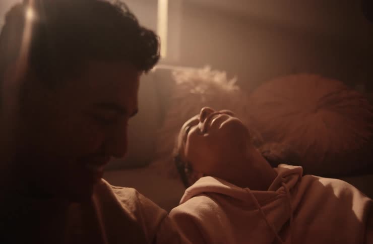 A young couple seated on the floor holding hands and laughing while resting their backs against the couch at midday