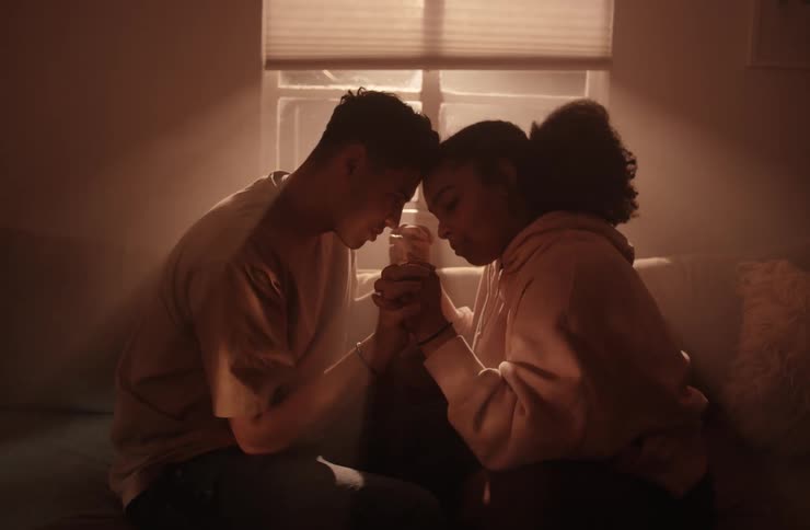 A young couple sits closely together holding hands with their foreheads touching the lighting is dim creating a warm intimate atmosphere as they connect in the quiet space