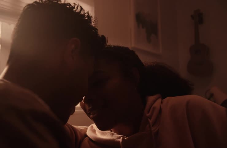 Cuddling couple smiles at each other and talks while near a window