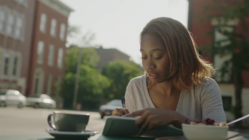 A woman is writing at a table with food