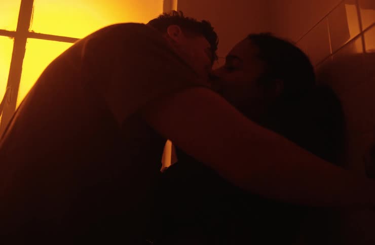 A warm dimlylit silhouetted shot of a man and a woman in an intimate embrace with the woman looking up and smiling at the man