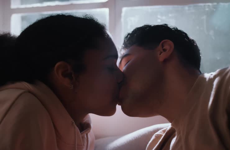 A couple is seen in a closeup shot leaning in and looking at each other affectionately they then share a kiss before pulling back slightly and continuing to smile at each other