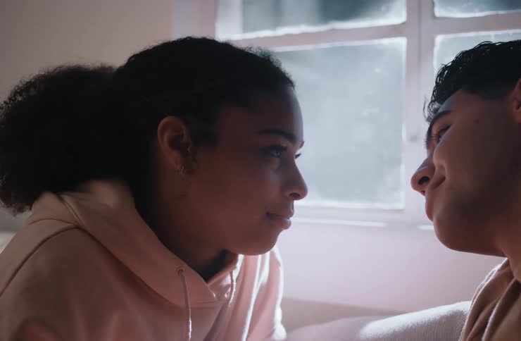 A young couple is sharing a gentle kiss in a closeup shot after the kiss they pull apart and look at each other with quiet affection their faces close together