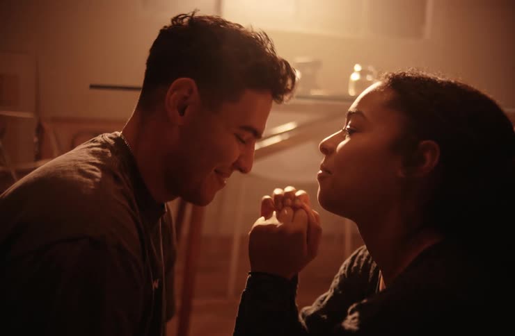A couple shares a kiss in their living room as they both smile afterward