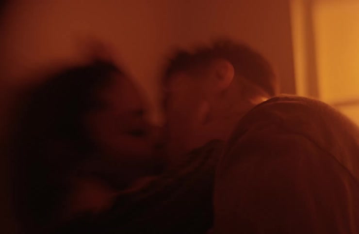 A warm and dimly lit outoffocus closeup shot of two people passionately kissing with their side profiles partially visible