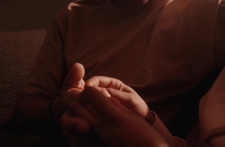 A closeup shot of a couple sitting together in a dimly lit room with the man speaking to the woman the camera focuses on their hands as they hold each others the man looks up and smiles at the woman