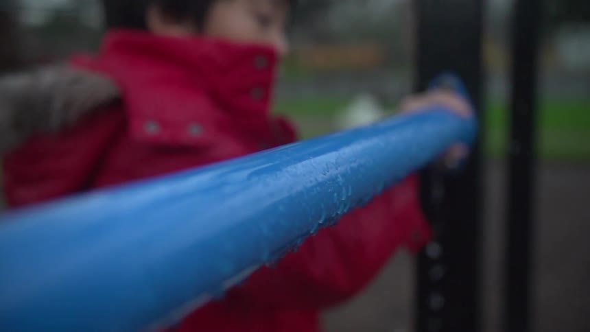 Boy holds onto a wet metal bar